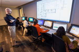 A professor looking over students working on an interior design project in a computer lab.