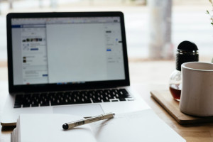 Pen and notebook sitting on a desk in front of a laptop with a coffee pot and mug to the right